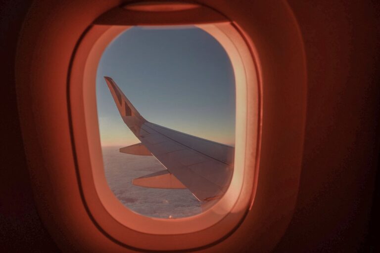 Крило на самолет през илюминатор на фона на залез по време на полет.