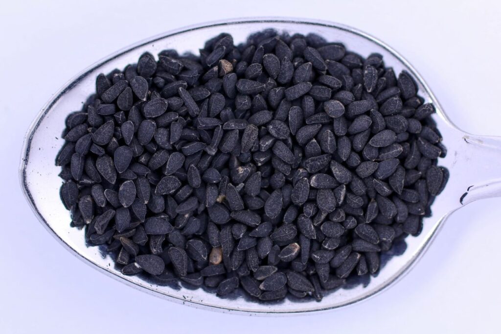 Черни семена на черен кимион (Nigella sativa) в метална лъжица на светъл фон.