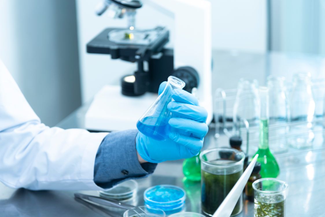 Free Scientist in gloves analyzing blue liquid in a laboratory setting with microscope and glassware. Stock Photo