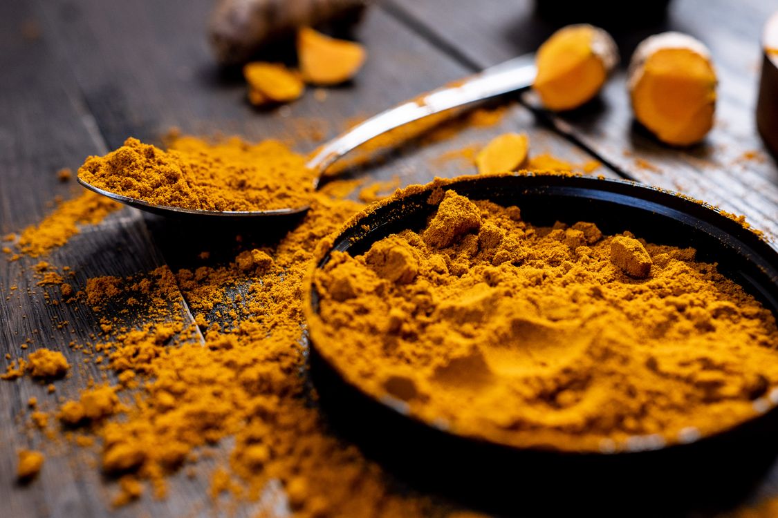 Free Close-up of vibrant turmeric powder with root on rustic wooden table, emphasizing texture and color. Stock Photo