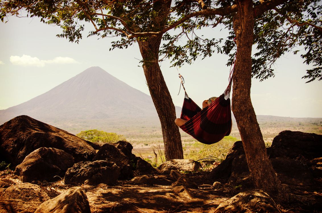 Free Person relaxing in a hammock between trees with a volcano in the background, capturing tranquility and nature. Stock Photo