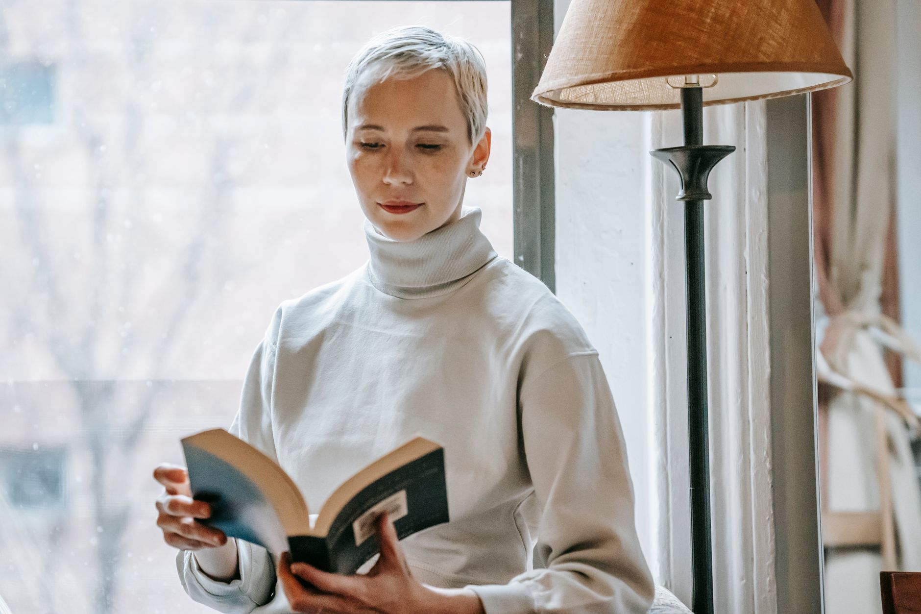Жена чете книга спокойно до прозорец на дневна светлина.